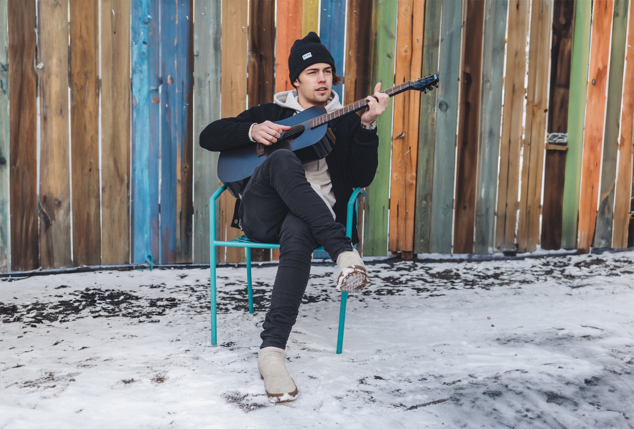 A young man plays a KLŌS Full Size Guitar in the snow 
