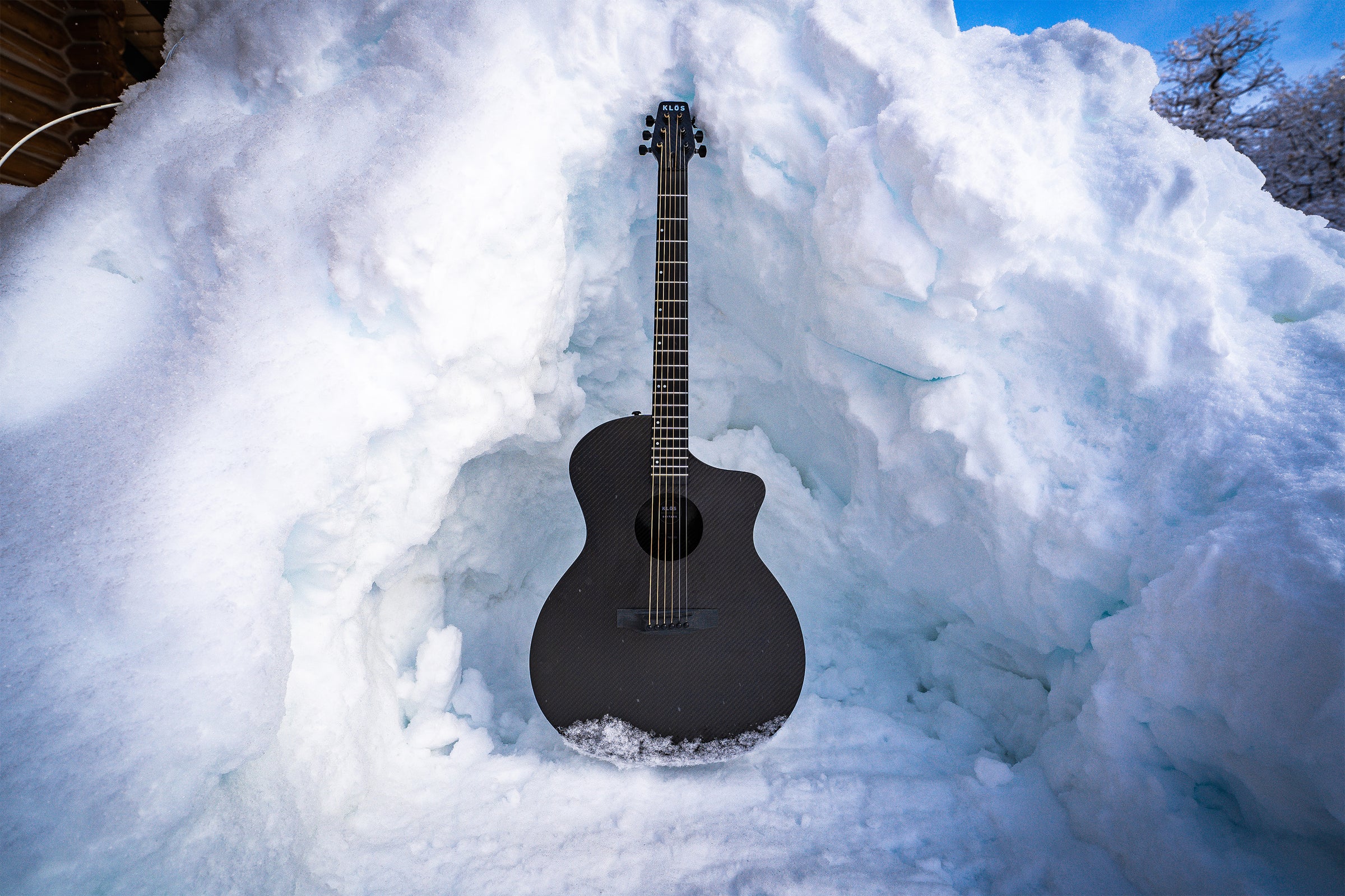 KLŌS grand cutaway sits in a snow fort, with some snow on the bottom of the body 