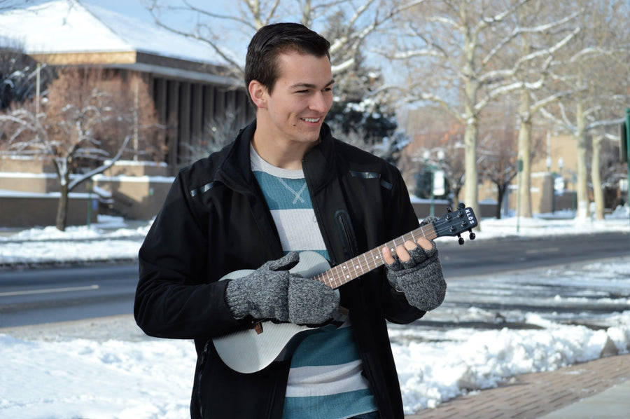 A young man plays the KLŌS Tenor Ukulele on the sidewalk during winter 