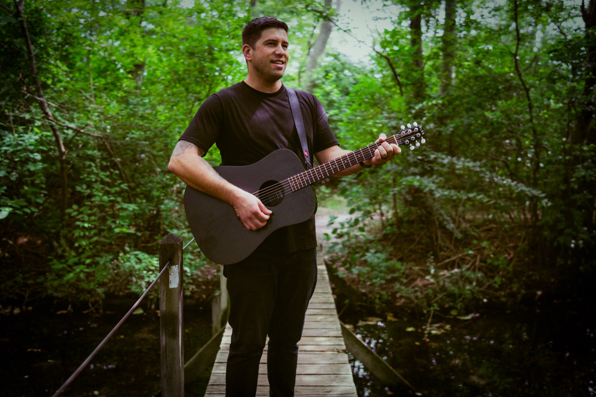 A man playing a KLŌS Full Size Guitar in a lush forest 