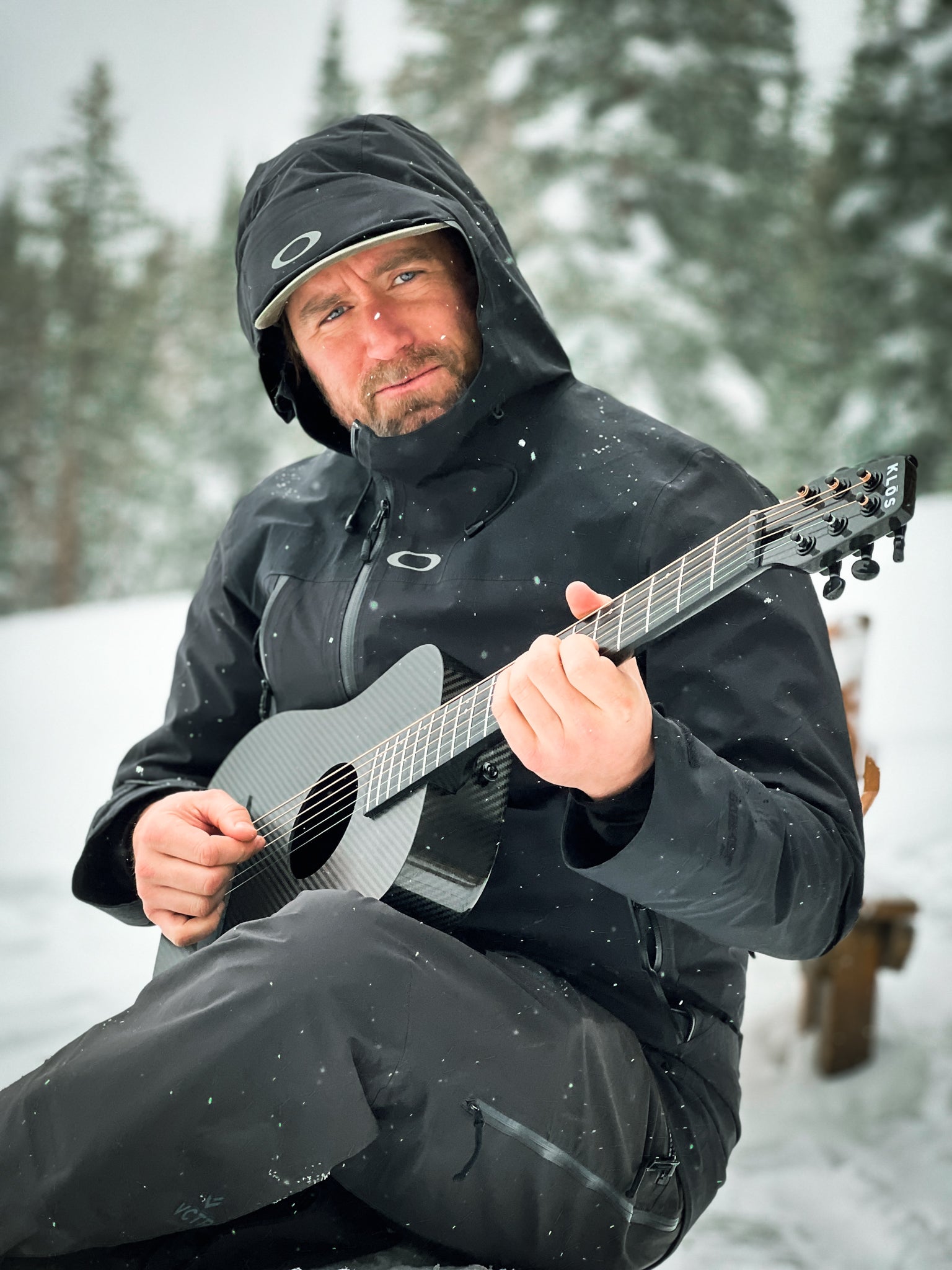 A man plays a KLŌS Full Carbon Travel while snow falls around him 