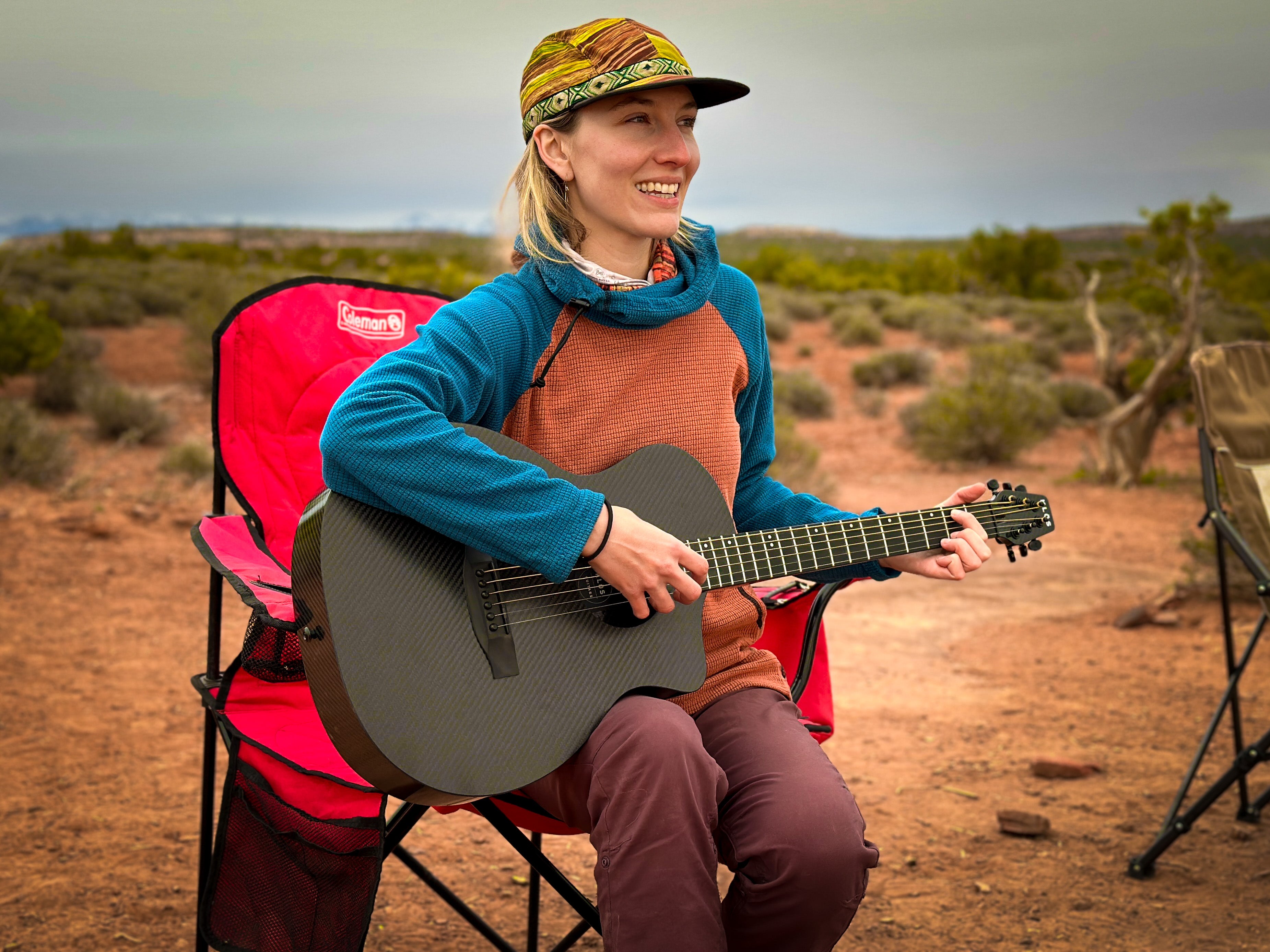 A woman plays the KLŌS cutaway guitar while camping in the desert 