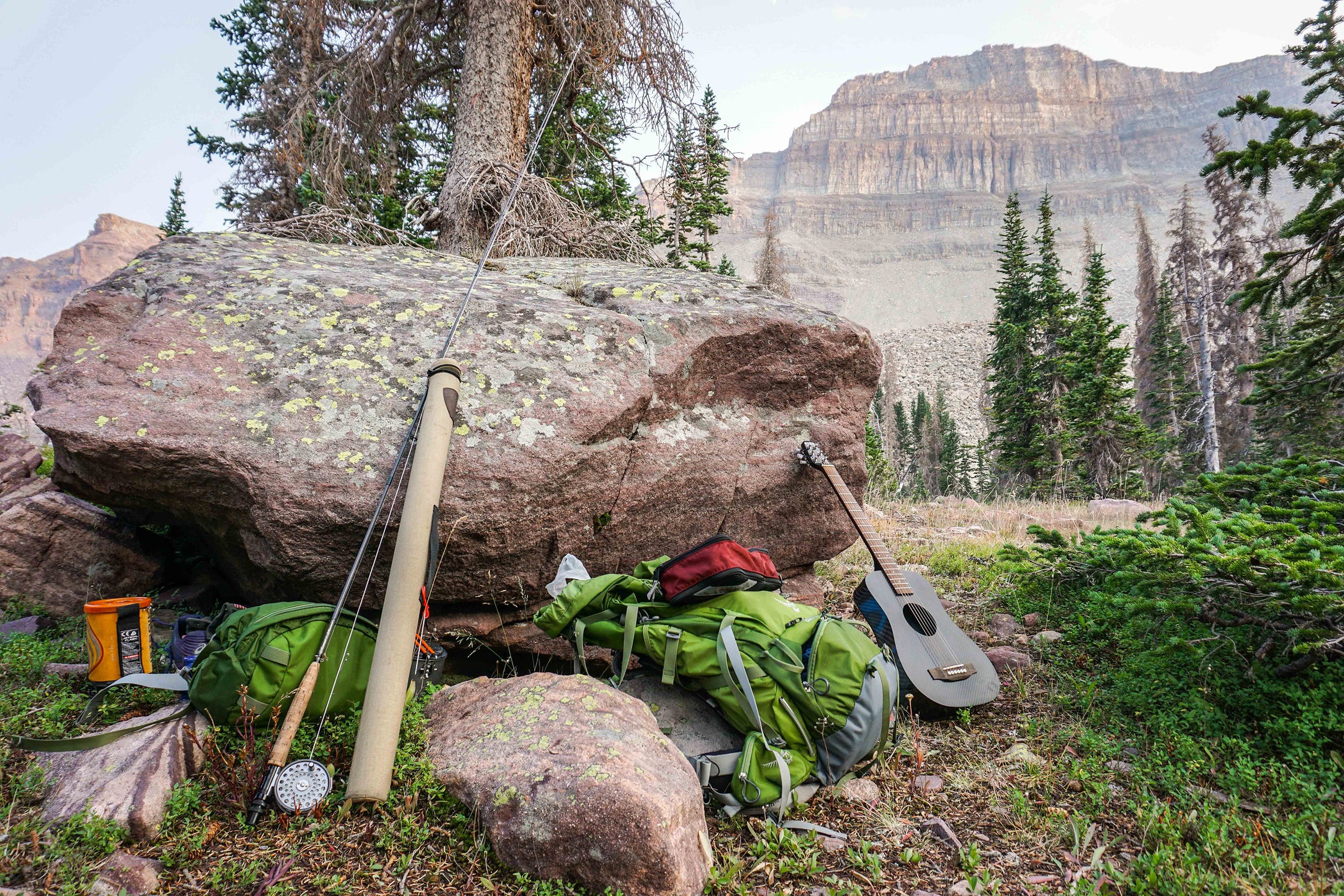A KLŌS Travel Guitar rests on a rock while surrounded by camping equipment 