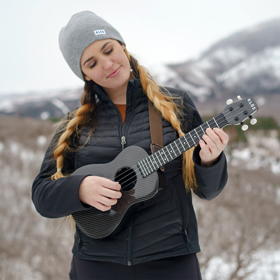 A woman plays the KLŌS Concert uke outside in the winter 